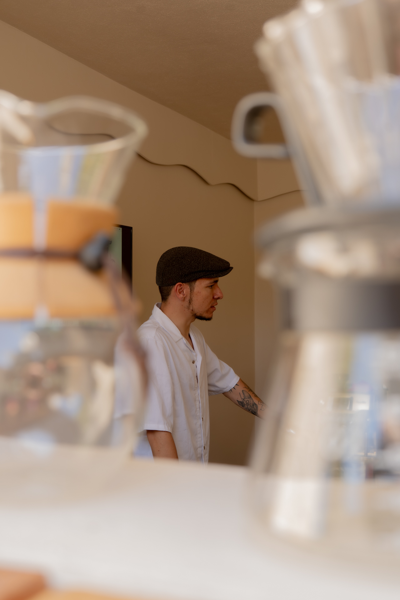 Instructor de barismo tatuado con gorra plana, perfil junto a las tazas